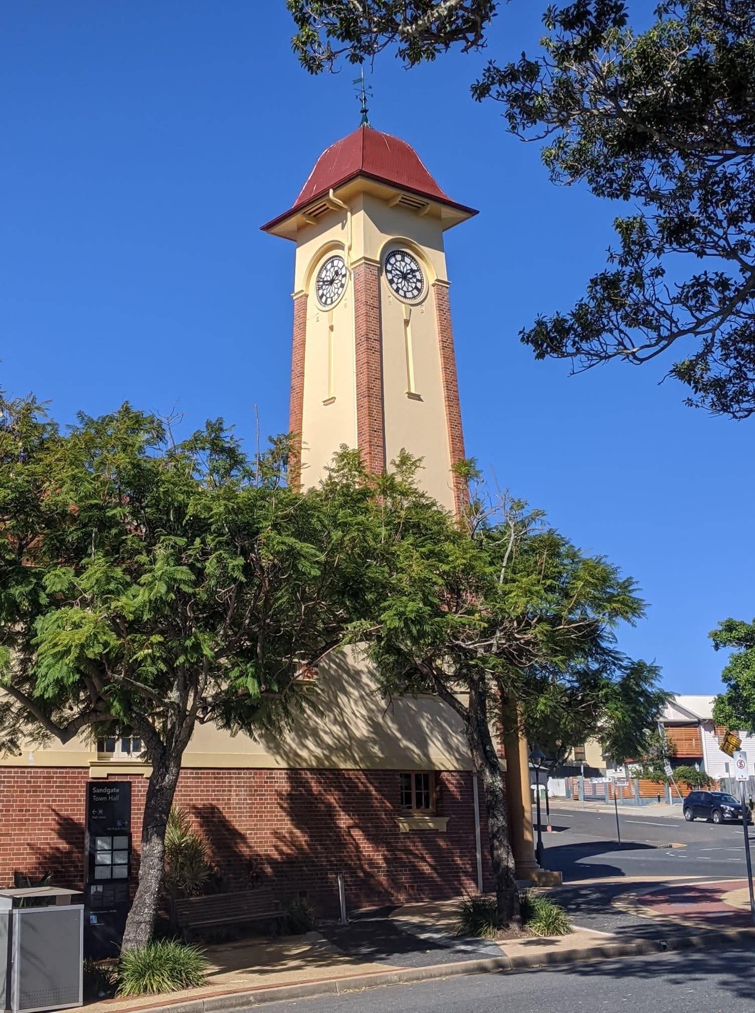 View of the Sandgate Town Hall clock tower with a tree in the foreground and clear blue sky in the background.